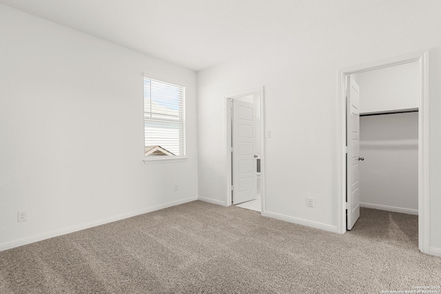 unfurnished bedroom featuring light carpet and a walk in closet