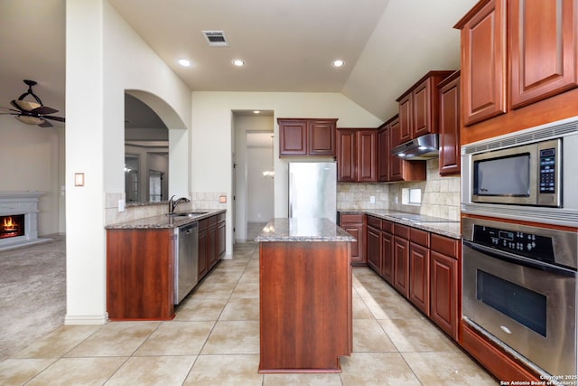 kitchen with sink, a kitchen island, stainless steel appliances, light stone counters, and light tile patterned flooring