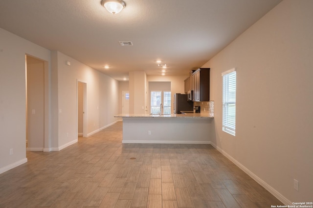 kitchen featuring light stone counters, tasteful backsplash, stainless steel refrigerator, kitchen peninsula, and light hardwood / wood-style floors