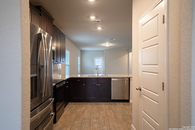 kitchen with sink, kitchen peninsula, stainless steel appliances, dark brown cabinets, and light hardwood / wood-style flooring