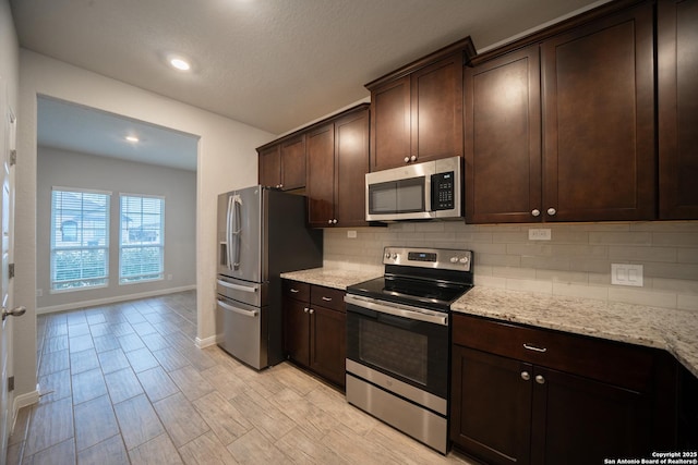 kitchen featuring tasteful backsplash, light stone countertops, appliances with stainless steel finishes, and dark brown cabinets