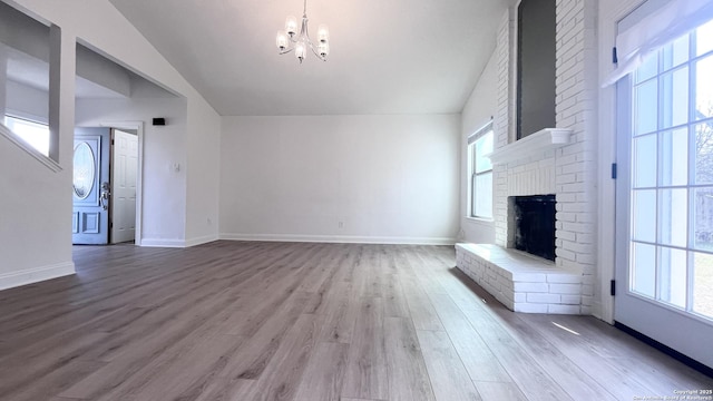 unfurnished living room with a brick fireplace, a healthy amount of sunlight, a chandelier, and light hardwood / wood-style floors