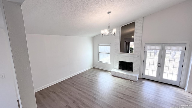 unfurnished living room featuring lofted ceiling, hardwood / wood-style floors, a notable chandelier, a textured ceiling, and a brick fireplace