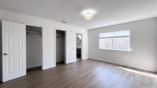 unfurnished bedroom with hardwood / wood-style flooring, ensuite bath, multiple closets, and a textured ceiling