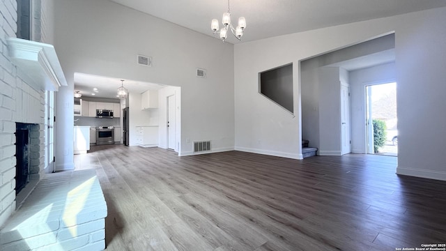 unfurnished living room featuring wood-type flooring, a brick fireplace, a notable chandelier, and high vaulted ceiling