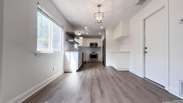 kitchen with appliances with stainless steel finishes, light wood-type flooring, white cabinets, hanging light fixtures, and an inviting chandelier