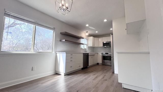 kitchen with decorative backsplash, light wood-type flooring, white cabinets, and appliances with stainless steel finishes