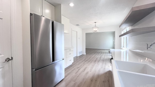 kitchen with sink, decorative light fixtures, a textured ceiling, stainless steel fridge, and white cabinets