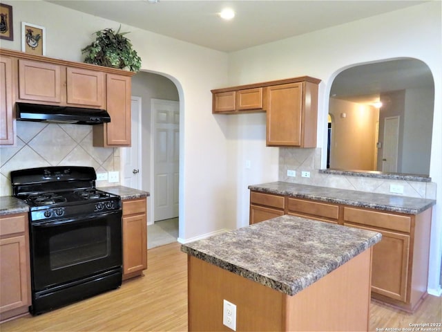 kitchen with black range with gas cooktop, light hardwood / wood-style flooring, a center island, and tasteful backsplash