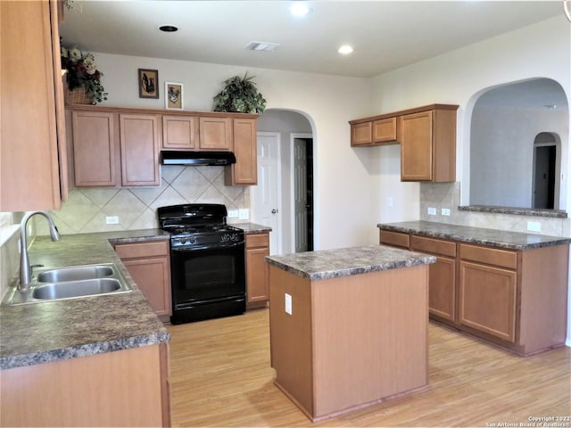 kitchen with a kitchen island, sink, decorative backsplash, light hardwood / wood-style floors, and gas stove