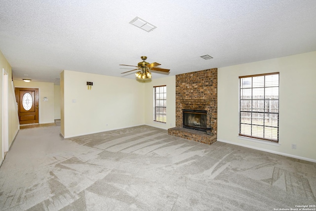 unfurnished living room with ceiling fan, a fireplace, light colored carpet, and a textured ceiling