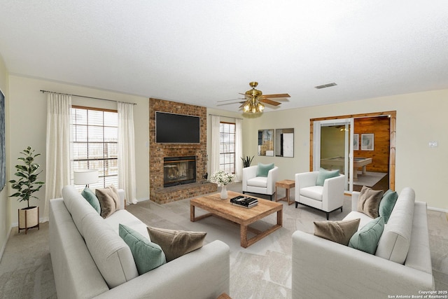 carpeted living room with a brick fireplace, a textured ceiling, and ceiling fan