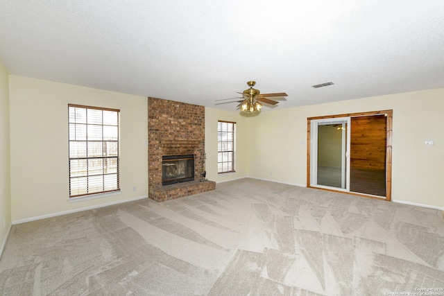 unfurnished living room featuring a brick fireplace, light colored carpet, a textured ceiling, and ceiling fan