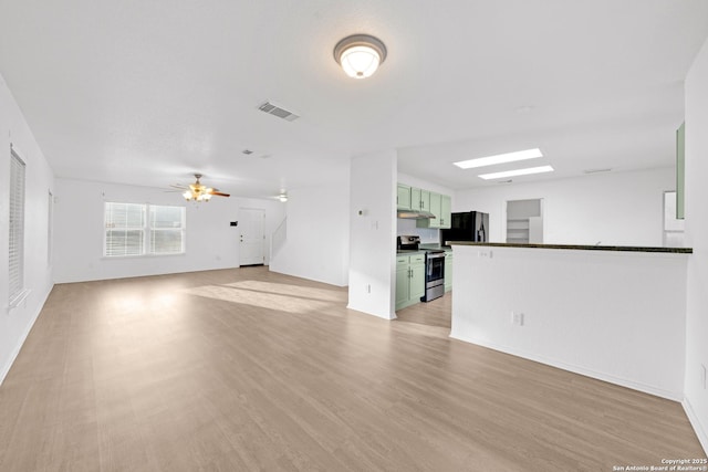 unfurnished living room with light hardwood / wood-style flooring, ceiling fan, and a skylight