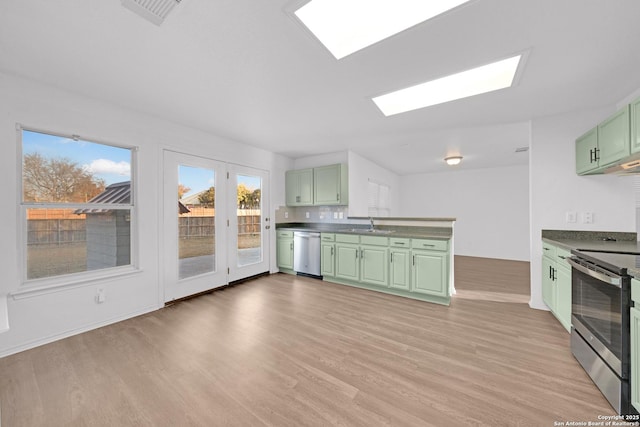 kitchen with a skylight, appliances with stainless steel finishes, light wood-type flooring, and green cabinetry