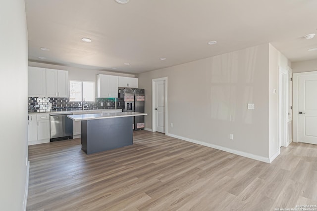 kitchen featuring tasteful backsplash, white cabinetry, a center island, stainless steel appliances, and light hardwood / wood-style flooring