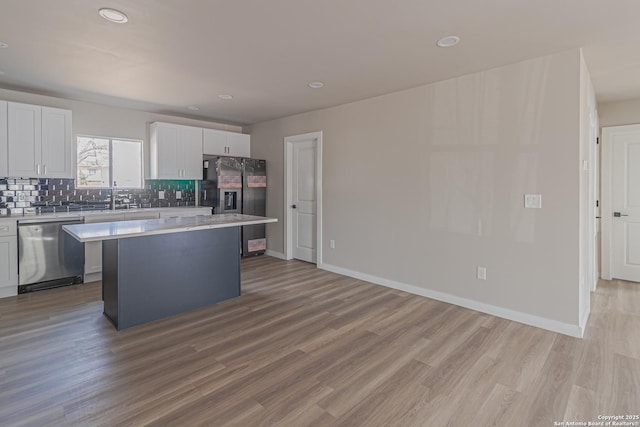 kitchen featuring white cabinetry, backsplash, stainless steel appliances, a kitchen island, and light wood-type flooring