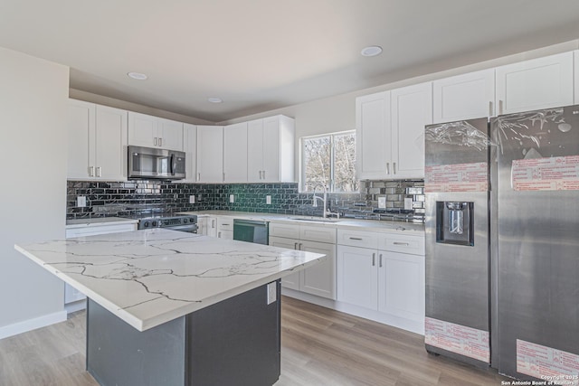 kitchen featuring sink, light stone counters, a center island, stainless steel appliances, and white cabinets