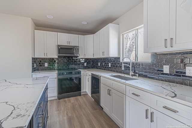 kitchen with sink, white cabinetry, black appliances, light stone countertops, and light wood-type flooring