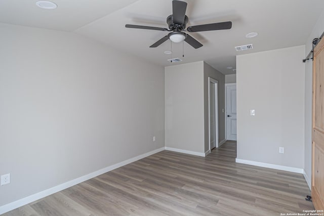 interior space with ceiling fan, a barn door, lofted ceiling, and light hardwood / wood-style floors