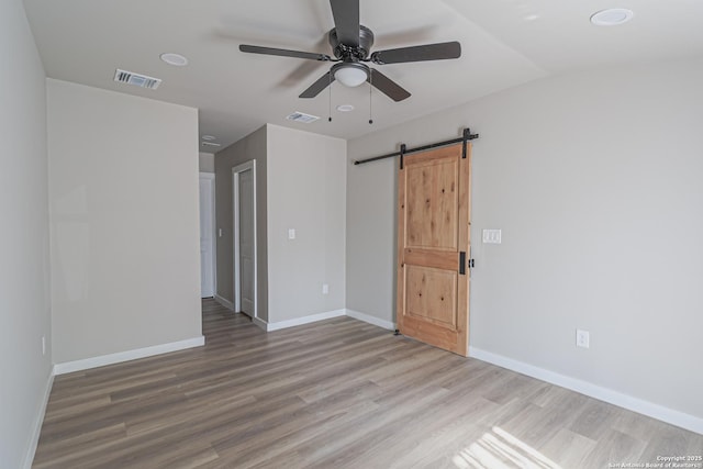 spare room featuring ceiling fan, lofted ceiling, a barn door, and light hardwood / wood-style floors