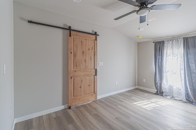 empty room with ceiling fan, a barn door, lofted ceiling, and light hardwood / wood-style floors