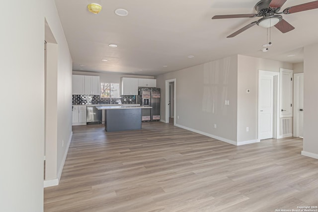 kitchen featuring appliances with stainless steel finishes, white cabinetry, a center island, tasteful backsplash, and light wood-type flooring