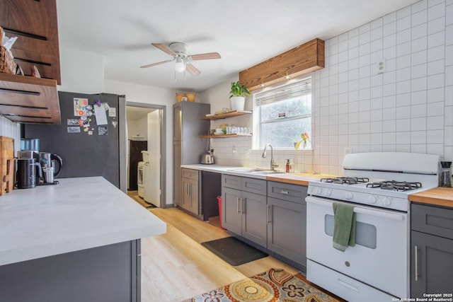 kitchen featuring sink, white gas range oven, gray cabinetry, tasteful backsplash, and light wood-type flooring