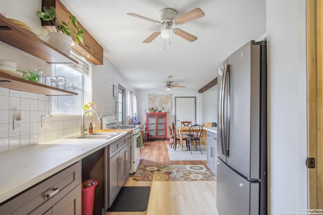 kitchen featuring sink, gas range gas stove, light hardwood / wood-style flooring, stainless steel fridge, and decorative backsplash