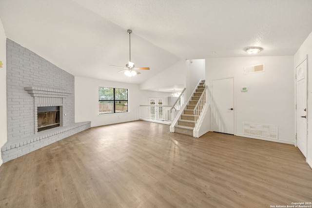 unfurnished living room featuring lofted ceiling, ceiling fan, light hardwood / wood-style floors, a textured ceiling, and a brick fireplace