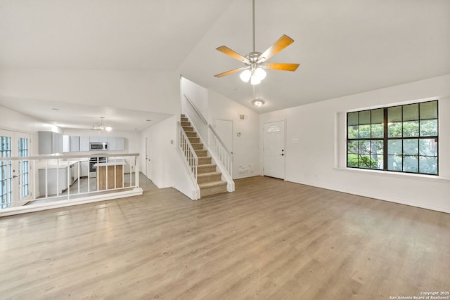 unfurnished living room with lofted ceiling, ceiling fan with notable chandelier, and light hardwood / wood-style floors