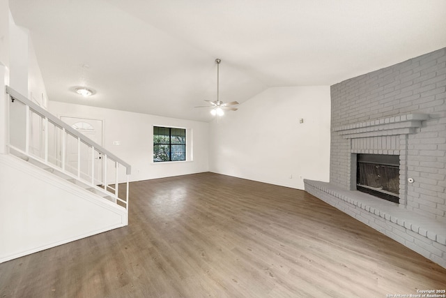 unfurnished living room featuring hardwood / wood-style flooring, ceiling fan, lofted ceiling, and a brick fireplace