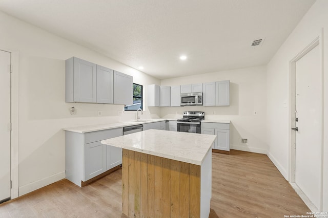 kitchen with light wood-type flooring, a kitchen island, gray cabinetry, and appliances with stainless steel finishes