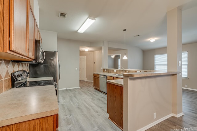 kitchen featuring light wood-type flooring, kitchen peninsula, pendant lighting, stainless steel appliances, and backsplash