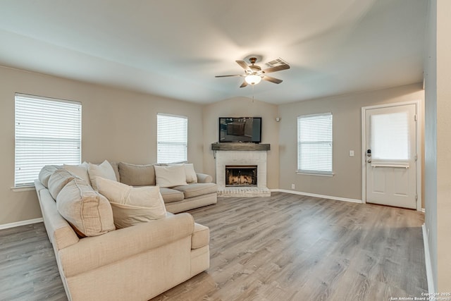 living room with ceiling fan, a brick fireplace, light hardwood / wood-style flooring, and a wealth of natural light