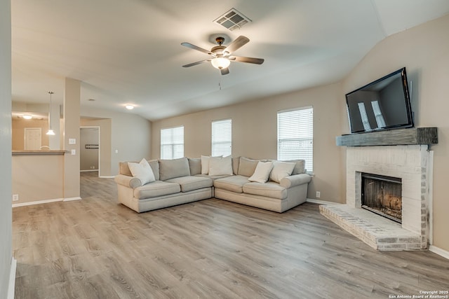 living room featuring a brick fireplace, vaulted ceiling, ceiling fan, and light wood-type flooring