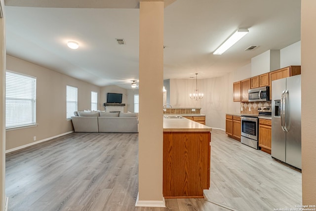 kitchen featuring decorative light fixtures, light wood-type flooring, a notable chandelier, stainless steel appliances, and backsplash