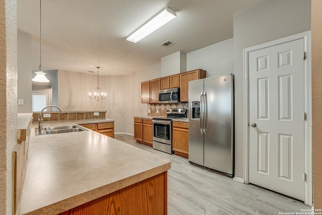 kitchen featuring appliances with stainless steel finishes, decorative light fixtures, sink, light hardwood / wood-style floors, and kitchen peninsula