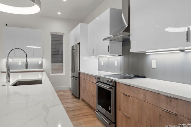 kitchen with white cabinetry, sink, stainless steel appliances, light stone countertops, and wall chimney exhaust hood