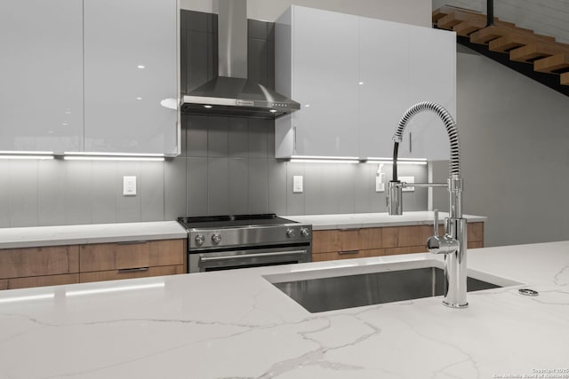 kitchen featuring light stone counters, wall chimney range hood, electric range, and white cabinetry