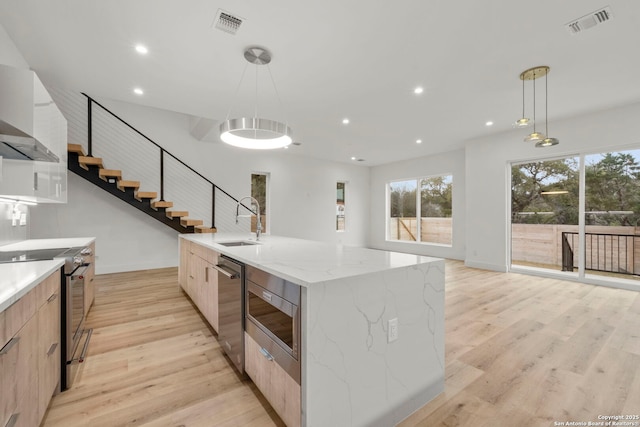 kitchen featuring a spacious island, sink, light stone counters, decorative light fixtures, and appliances with stainless steel finishes