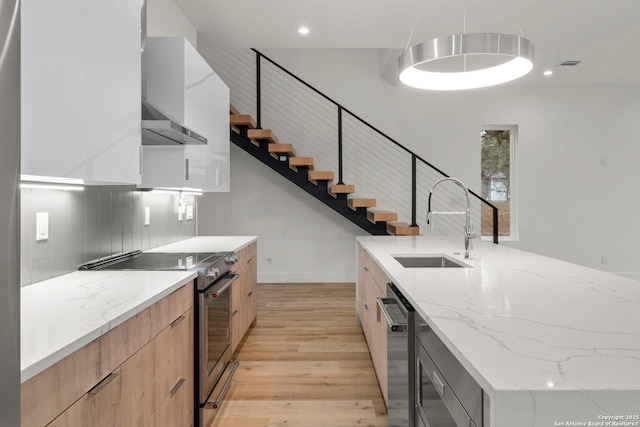 kitchen featuring appliances with stainless steel finishes, sink, light stone counters, wall chimney range hood, and light hardwood / wood-style flooring