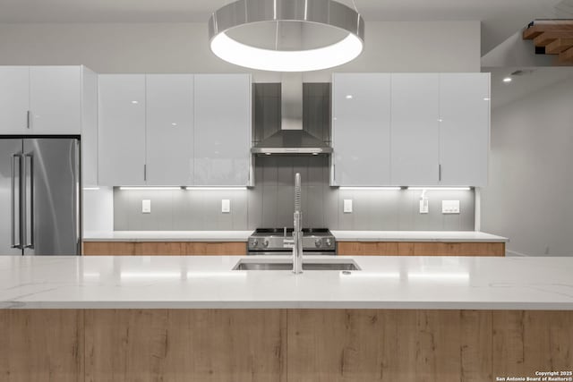 kitchen with high quality fridge, wall chimney range hood, white cabinets, and light stone counters