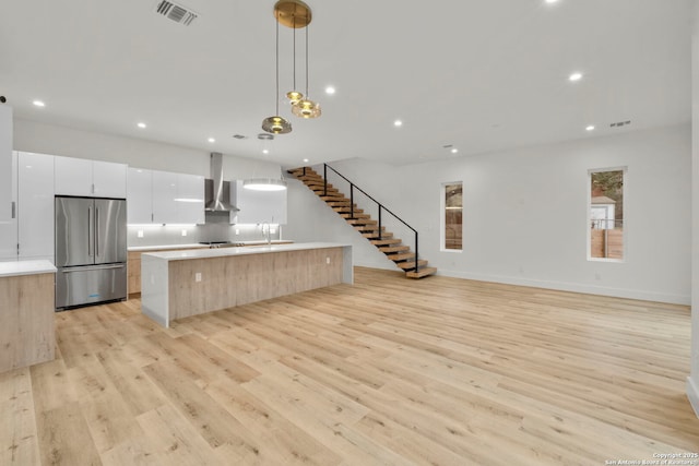 kitchen featuring white cabinetry, hanging light fixtures, a large island with sink, stainless steel refrigerator, and light hardwood / wood-style floors