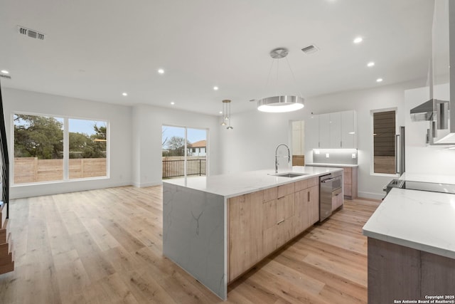 kitchen featuring light stone counters, hanging light fixtures, light brown cabinetry, and a large island with sink