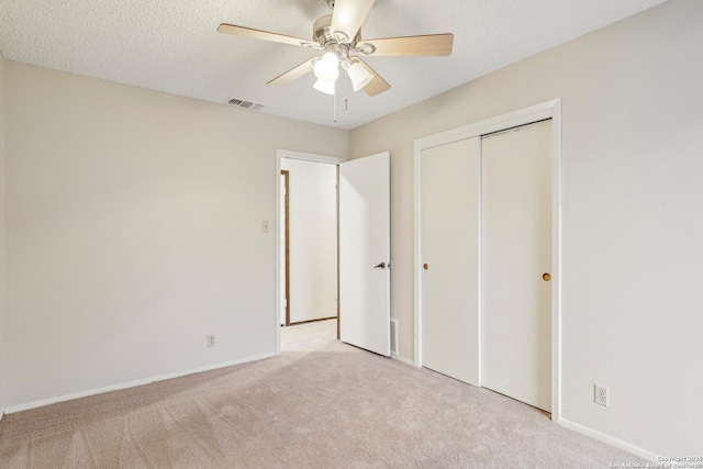 unfurnished bedroom with light carpet, ceiling fan, a closet, and a textured ceiling