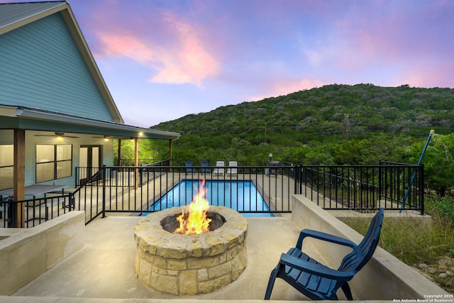 pool at dusk featuring a patio area, ceiling fan, and a fire pit