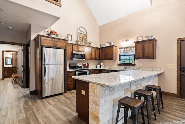 kitchen with a breakfast bar area, hardwood / wood-style floors, stainless steel appliances, light stone countertops, and kitchen peninsula