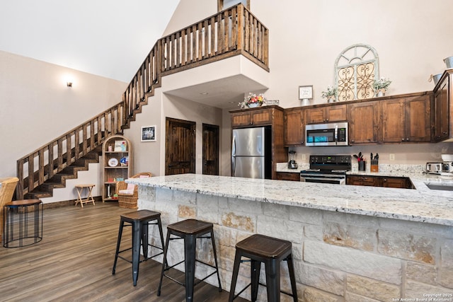 kitchen with dark wood-type flooring, a breakfast bar area, appliances with stainless steel finishes, high vaulted ceiling, and light stone counters