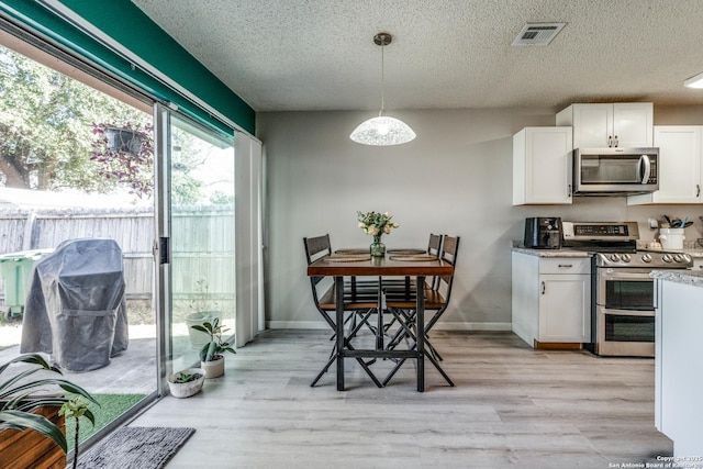 kitchen featuring pendant lighting, stainless steel appliances, light wood-type flooring, and white cabinets